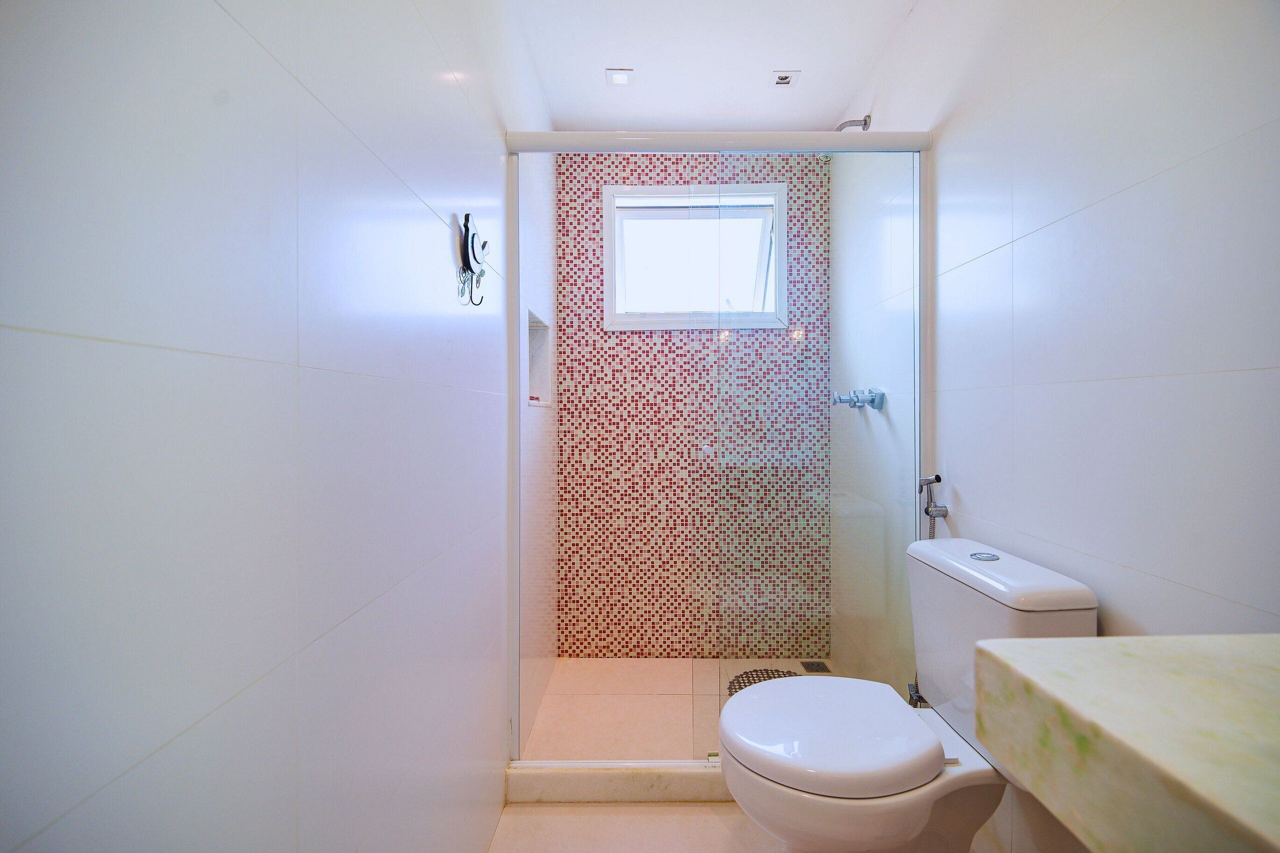 Een kleine badkamer met douche, toilet en een klein raam.