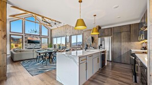 A modern kitchen with a large island, wooden cabinets, and pendant lighting.