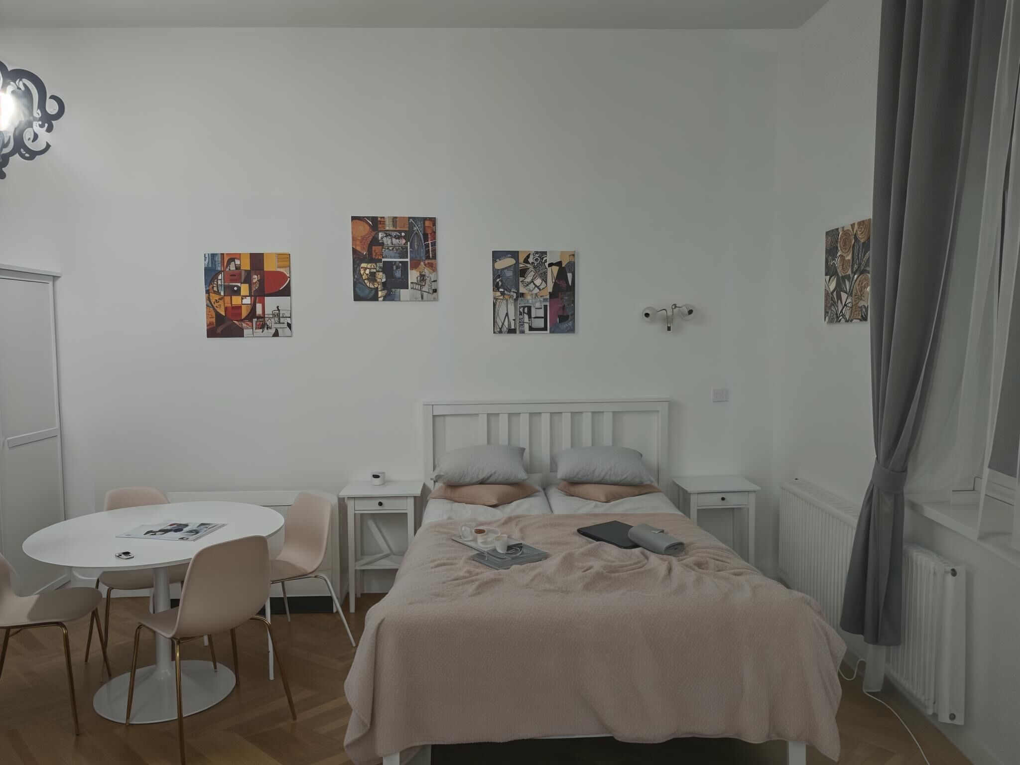 A bedroom with a bed, bedside tables, a chair, and a small round table. There are three artworks on the wall.