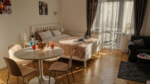 A modern hotel room with a bed, bedside table, and a round dining table with chairs.