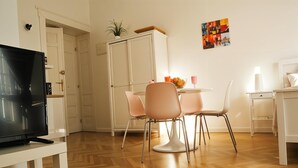 A modern living room with a flat-screen TV, a dining area with a table and chairs, and a white cabinet.