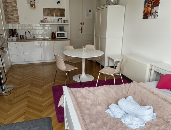 A modern, well-lit room with a dining table, chairs, a bed with a pink blanket, a white wardrobe, and a kitchen area with a microwave and sink. - Cracow Route #1 - Old Town (Kraków)