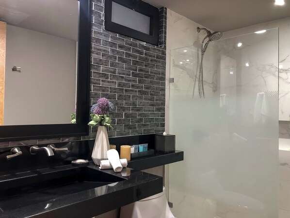 Une salle de bain moderne avec un lavabo noir, un miroir, un vase de fleurs et une cabine de douche en verre.