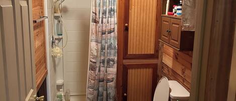 A compact wooden bathroom with a shower, toilet, and storage cabinet.