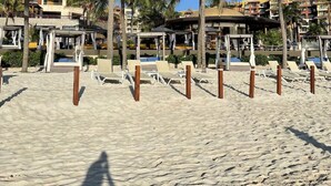 Una playa con palmeras, sillas de descanso y un edificio con balcones.