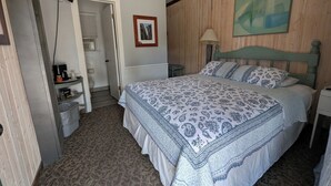 A bedroom with a bed, a television, a painting, and a door leading to a bathroom. - Squaw Valley Motel Room #3 (Yokuts Valley)