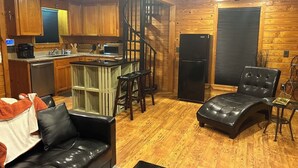 A cozy cabin interior with a kitchen, a dining area, a living room with a sofa and a lounge chair, and a wooden staircase. - Cozy cabin with 1 bedroom, Lakefront views in tranquil Terry! (Terry)