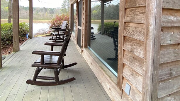 A wooden cabin with a covered porch, rocking chairs, and a view of a lake. - Cozy cabin with 1 bedroom, Lakefront views in tranquil Terry! (Terry)