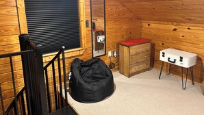 A wooden-paneled room with a window, a mirror, a dresser, a suitcase, and a black bean bag. - Cozy cabin with 1 bedroom, Lakefront views in tranquil Terry! (Terry)