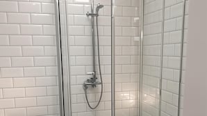 Ein modernes Badezimmer mit einer gläsernen Duschkabine, weißen Fliesen im U-Bahn-Format und einem Schachbrettmuster auf dem Boden.