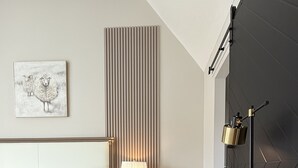 A modern hotel room with a bed, bedside lamp, bedside table, and a desk with a lamp.