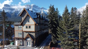 A multi-story lodge with a prominent entrance and a view of snow-covered mountains.
