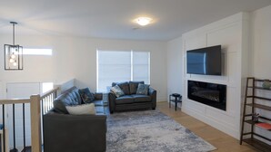 A modern living room with two sofas, a fireplace, a TV mounted on the wall, and a staircase leading to another level.