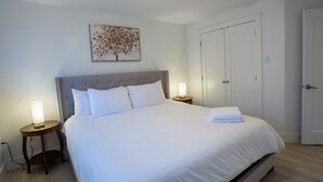 A neatly made bed with white linens, a headboard, two bedside lamps, and a wall-mounted artwork.
