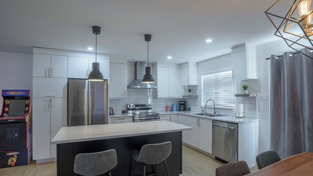 A modern kitchen with a central island, stainless steel appliances, pendant lighting, and a dining area with bar stools.