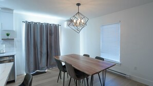 A modern kitchen with a dining area, featuring a wooden table, chairs, and a geometric pendant light.