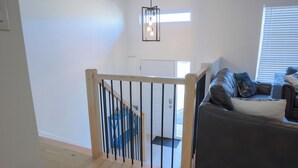 A modern living room with a grey sofa, a wooden staircase with blue railings, and a hanging light fixture.