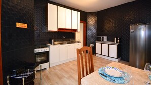 Une cuisine compacte équipée d’une cuisinière, d’un four, d’un four à micro-ondes et d’un réfrigérateur. On y trouve une table à manger avec une chaise et une assiette.
