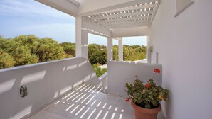 A white balcony with a pergola, a potted plant with red flowers, and a view of greenery. - Studio in Perissa beach for 4 people (thira)