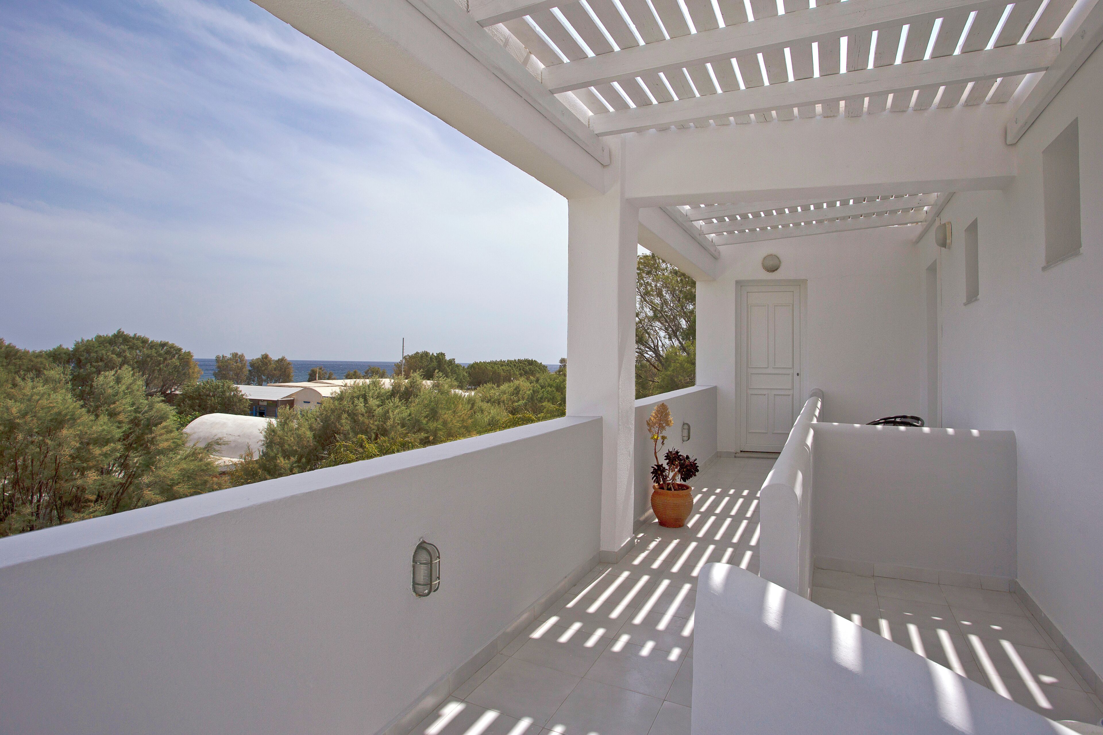 Ein weißer Balkon mit Blick auf Bäume und das Meer.