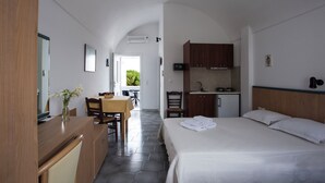 A bedroom with a bed, a desk, a chair, a small kitchenette, and a bathroom. - Studio in Perissa beach for 4 people (thira)
