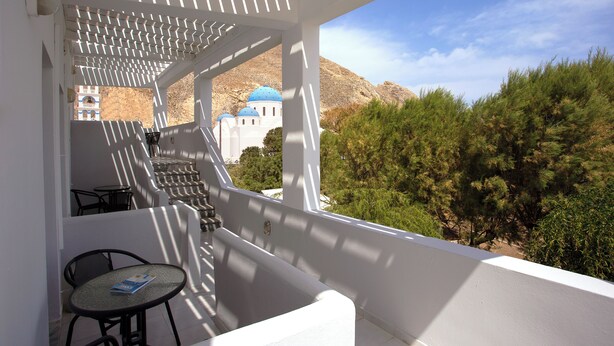 A balcony with a table and chairs, overlooking a building with blue domes and a mountainous landscape. - Studio in Perissa beach for 4 people (thira)