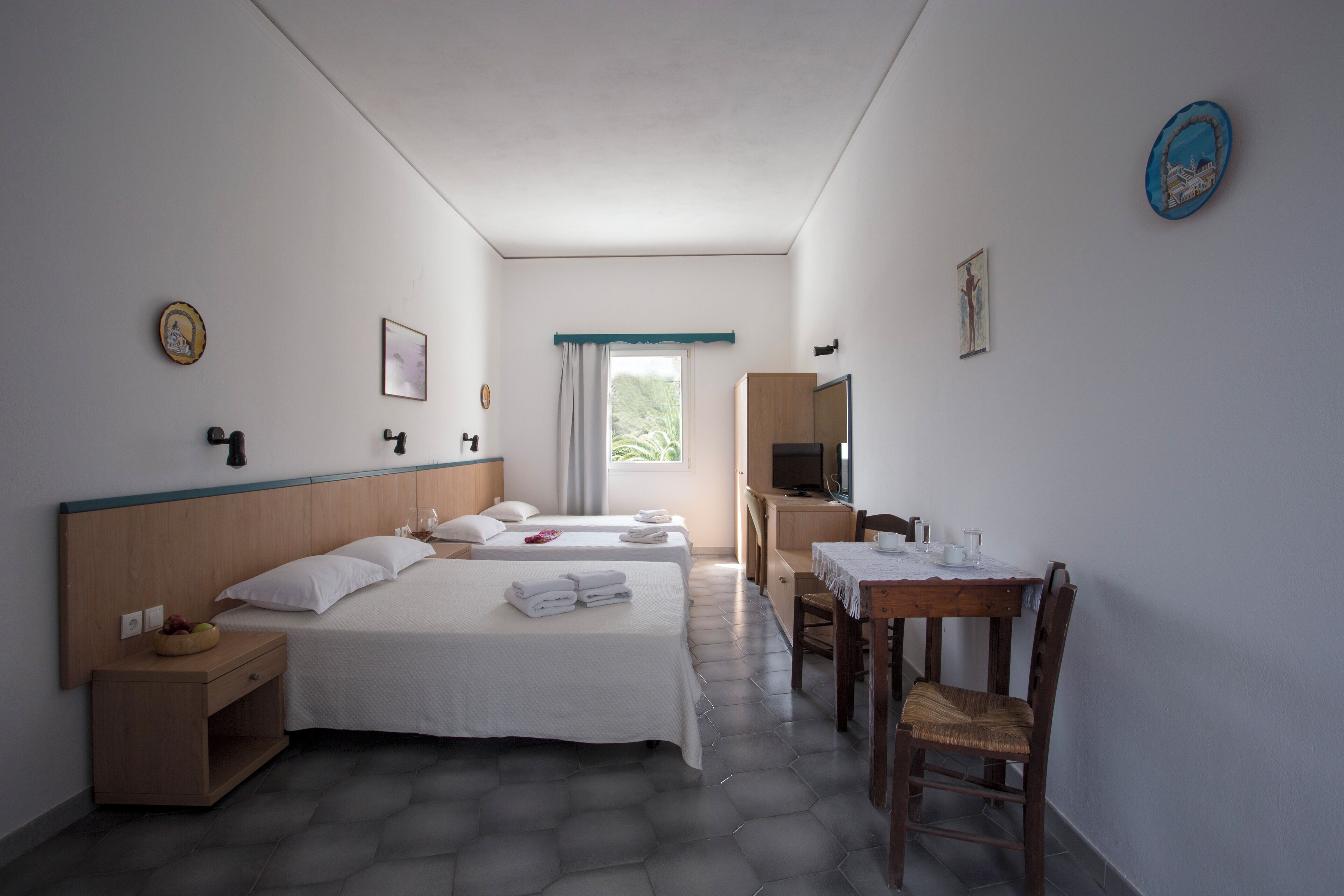 Ein Hotelzimmer mit zwei Betten, einem Schreibtisch, einem Stuhl, einem Fernseher und einem Fenster mit Vorhängen.