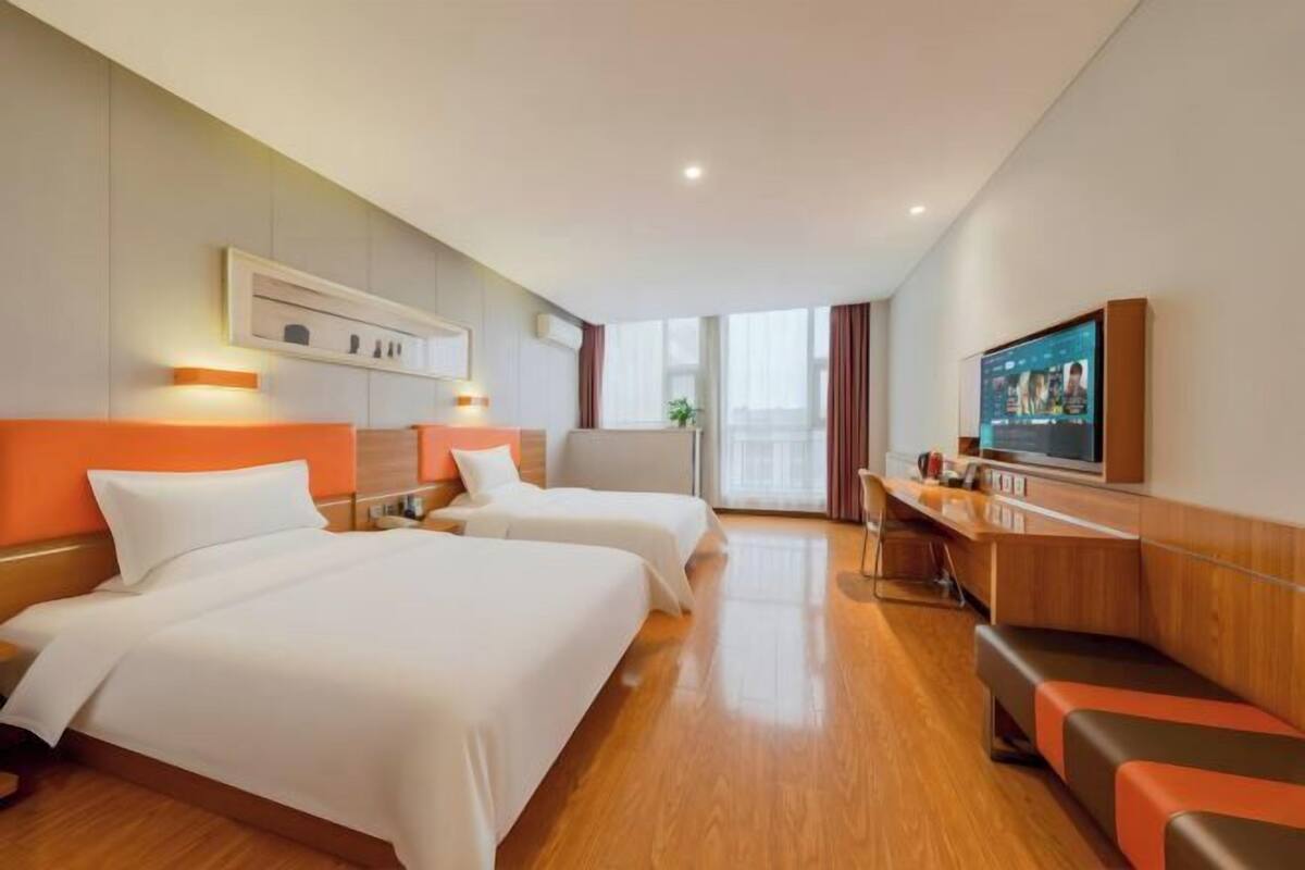 A hotel room with two beds, a desk, a TV, and a window.