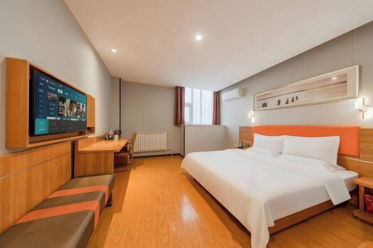 A hotel room with a bed, a desk, a TV, and a seating area.