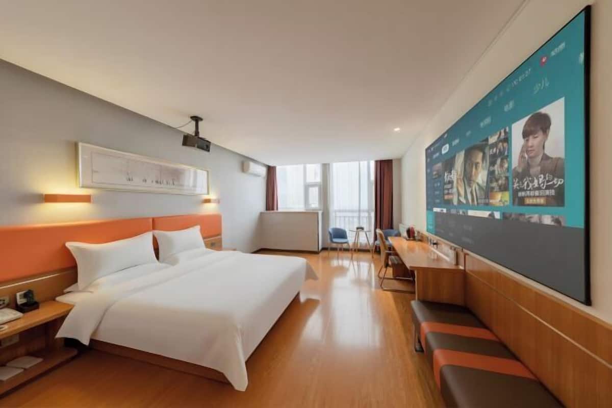 A hotel room with a bed, a desk, a chair, a TV screen, and a window.