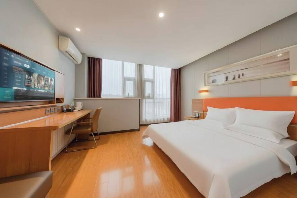 A hotel room with a bed, a desk, a television, and a window with curtains.