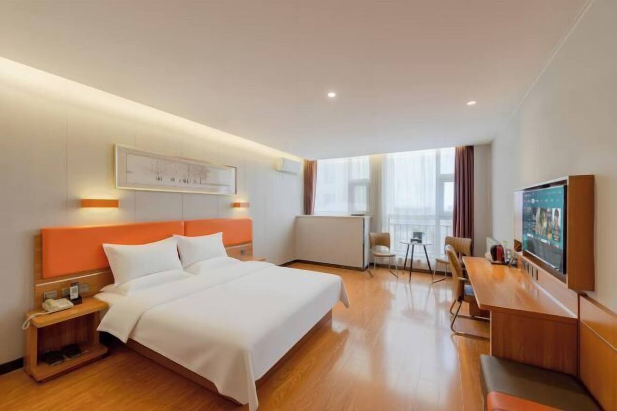 A hotel room with a bed, bedside table, TV, and a desk with a chair.