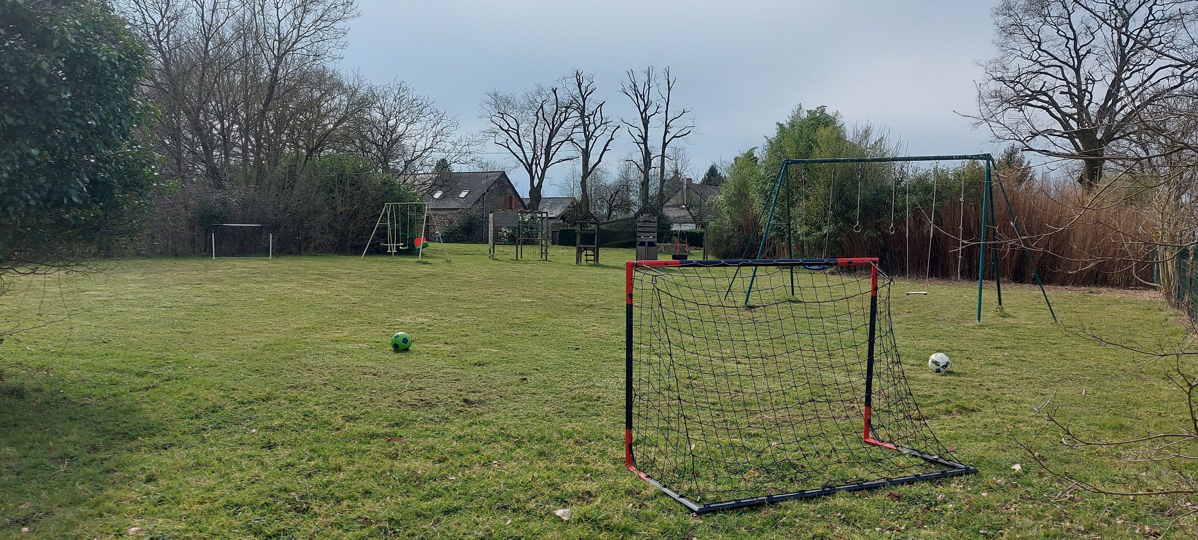 A grassy field with a soccer goal and swings.
