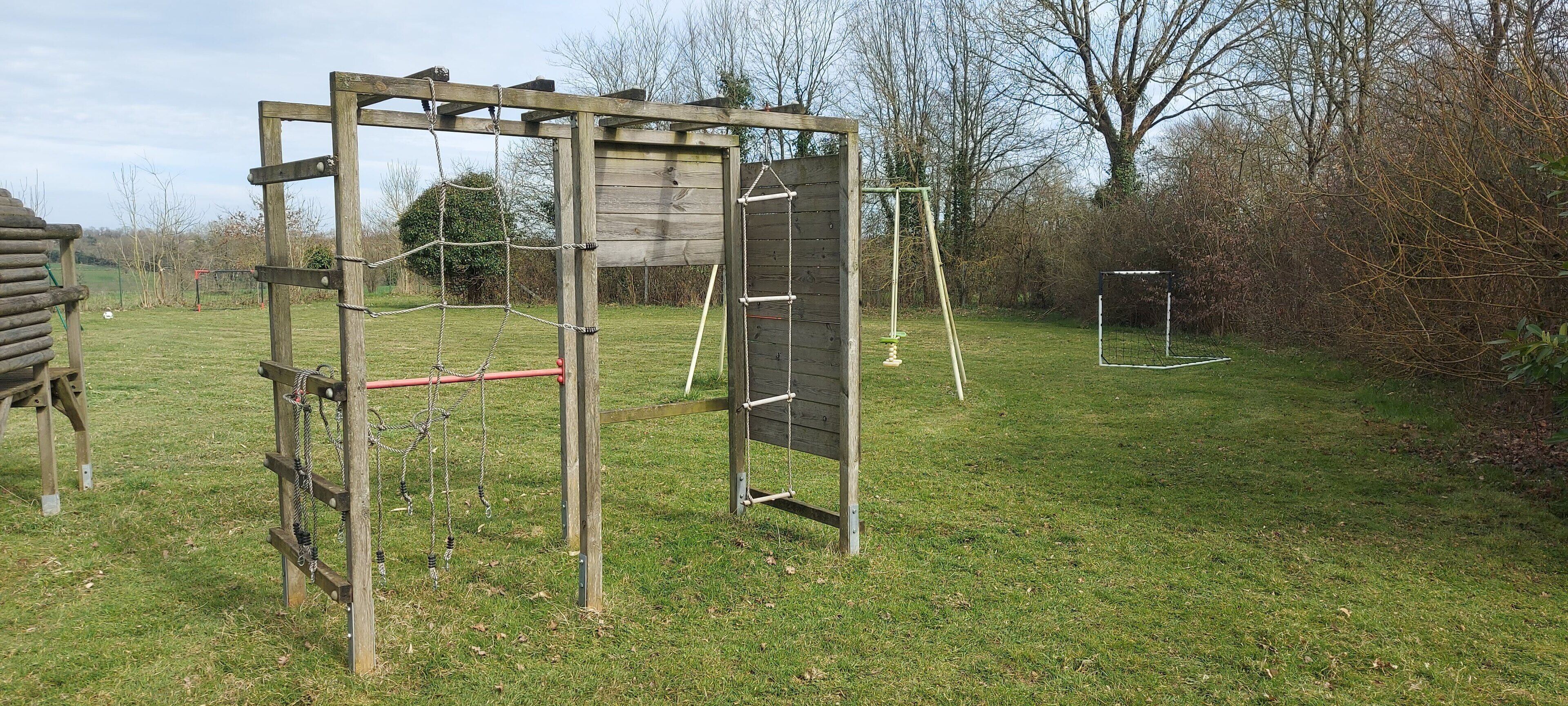 A wooden play structure in a grassy yard with a swing set and a climbing frame.