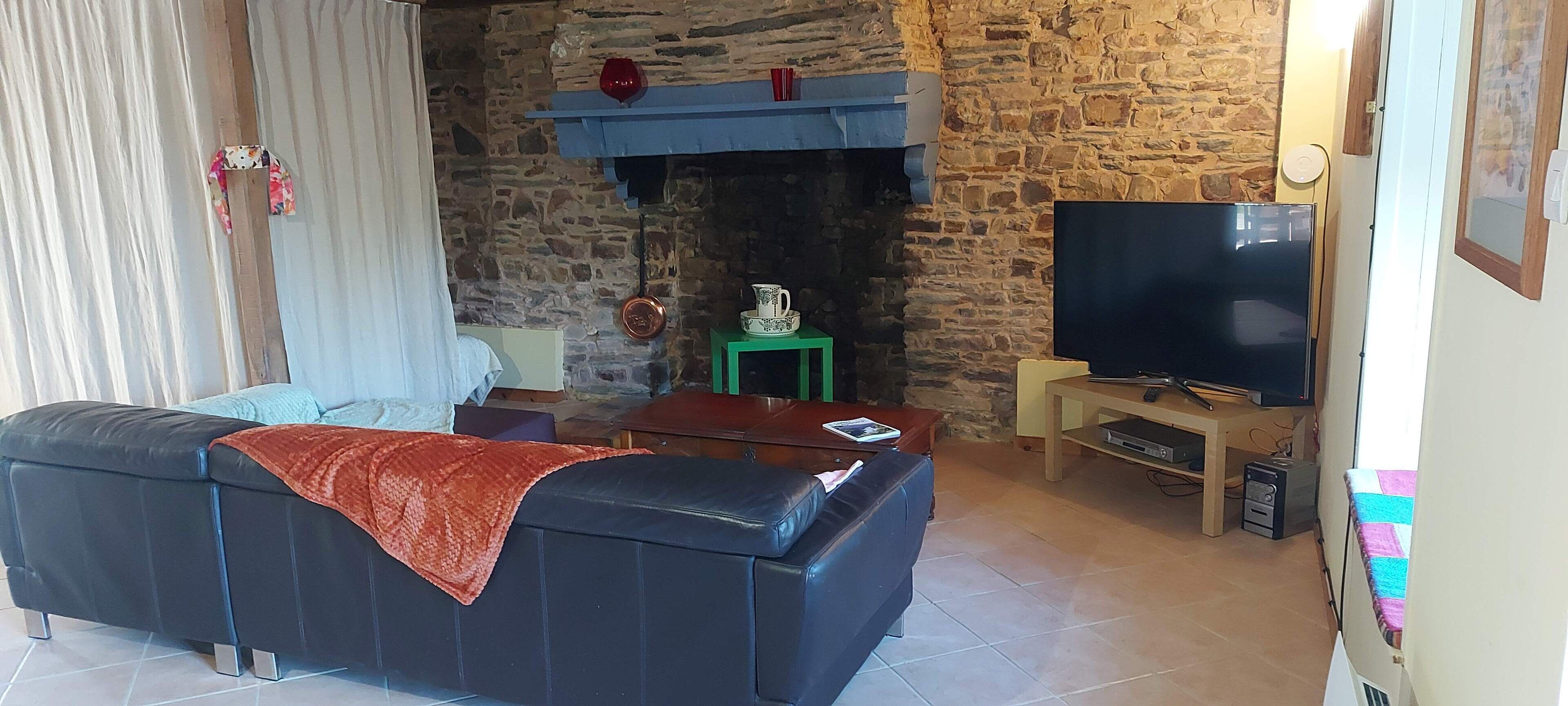 Sala de estar com parede de pedra, sofá de couro preto, televisão e lareira.