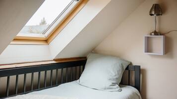 Une chambre avec un plafond en pente, un puits de lumière, un lit avec une tête de lit, une table de chevet et une lampe fixée au mur.