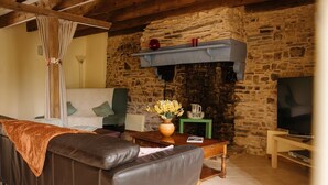 A cozy living room with a stone fireplace, a leather sofa, a television, and a vase with flowers. - Mézon Maëlle, ideal for families and friends (Teillay)