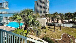 Ein Balkon mit Pool, Palmen und Blick auf ein hohes Gebäude über dem Wasser.