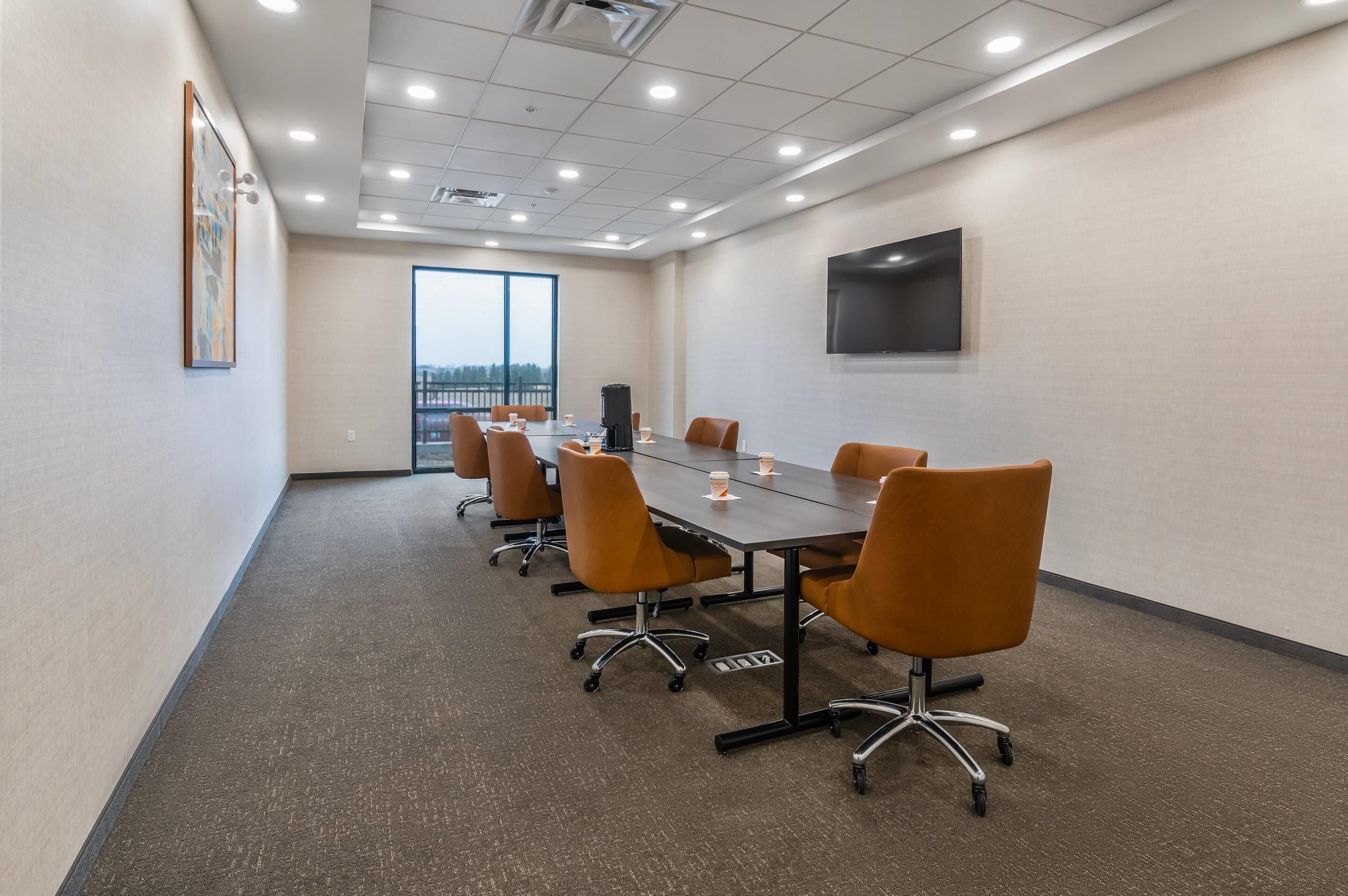 A conference room with a long table, orange chairs, a projector, and a TV on the wall.