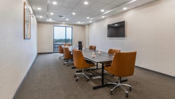 A conference room with a long table, orange chairs, a projector, and a TV on the wall.