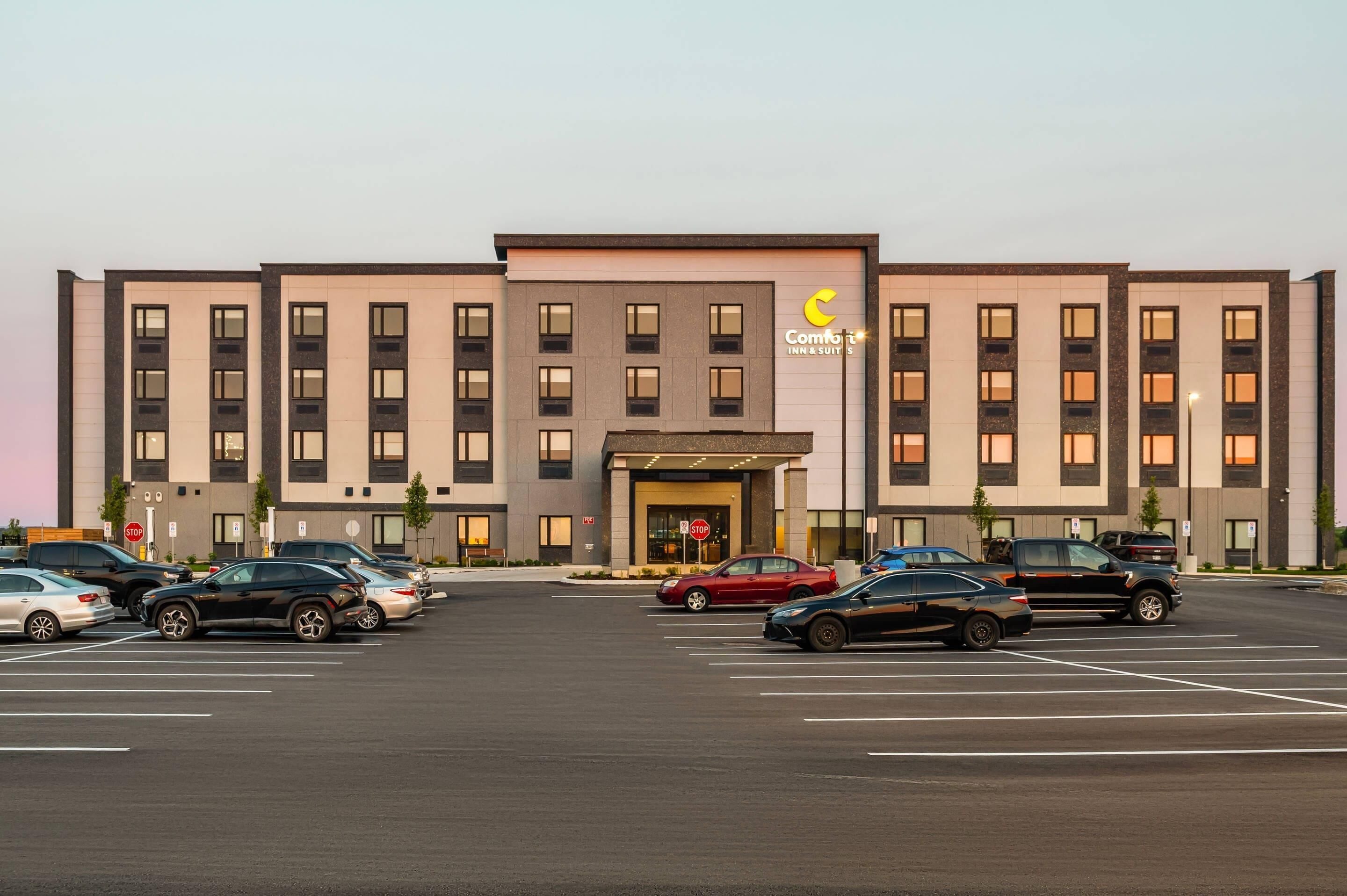 Un hotel con fachada moderna, un estacionamiento con varios coches y una señal de parada al frente.