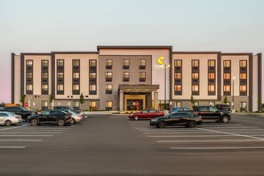 A hotel with a modern facade, a parking lot with several cars, and a stop sign in front.
