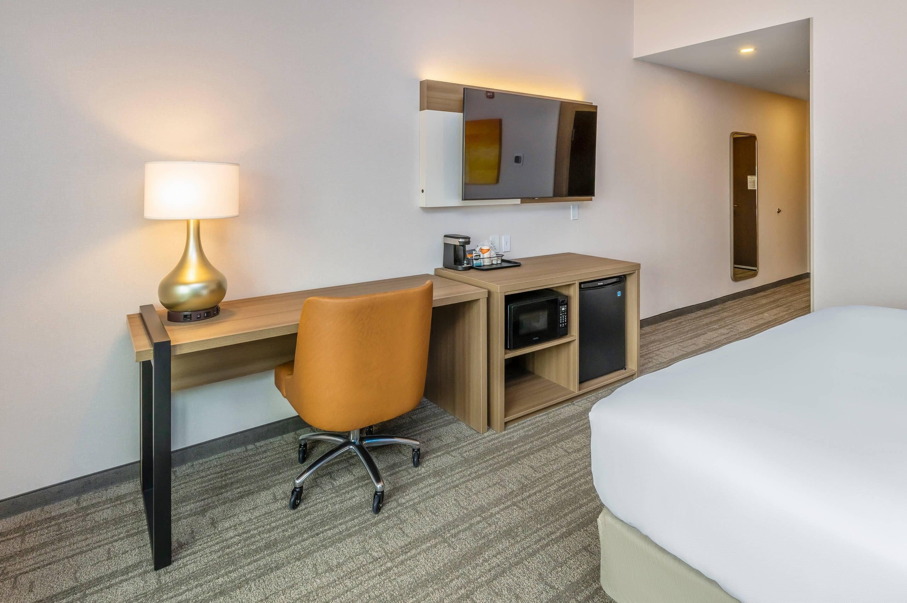 Hotellihuone, jossa on sänky, työpöytä lampun kanssa, mikroaaltouuni ja pieni kaappi.
