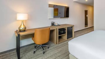 Hotellihuone, jossa on sänky, työpöytä lampun kanssa, mikroaaltouuni ja pieni kaappi.
