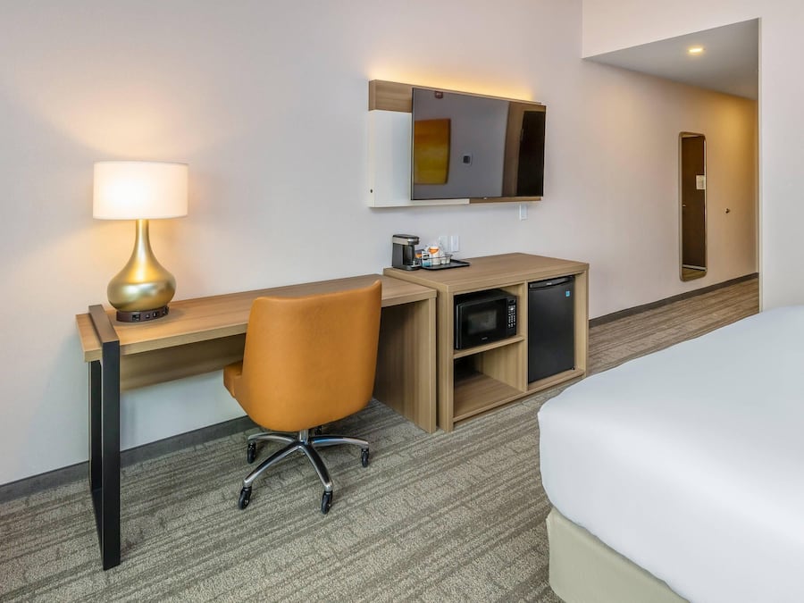 Hotellihuone, jossa on sänky, työpöytä lampun kanssa, mikroaaltouuni ja pieni kaappi.
