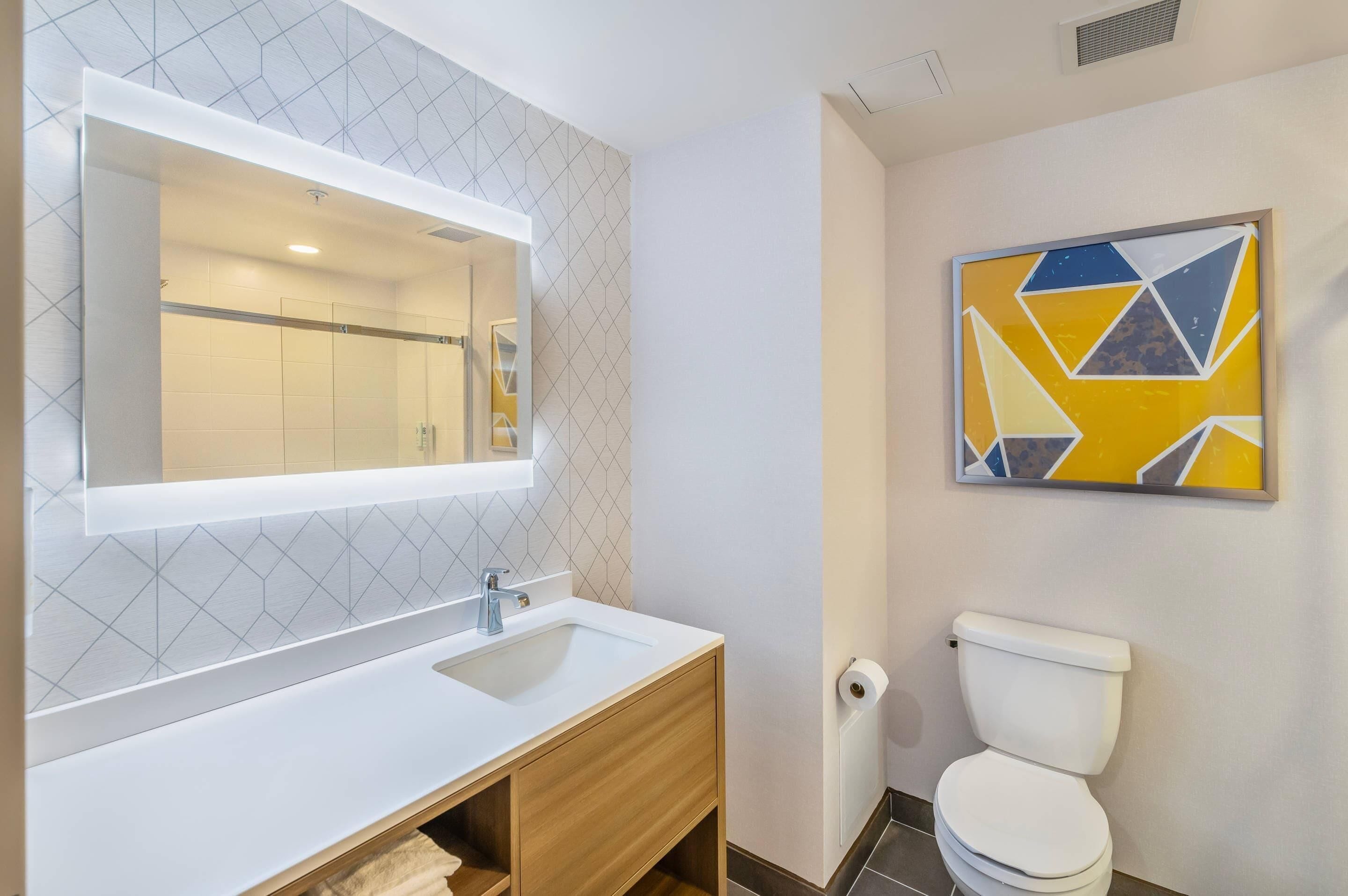 A bathroom with a white sink, a mirror, a toilet, and a geometric wall art piece.