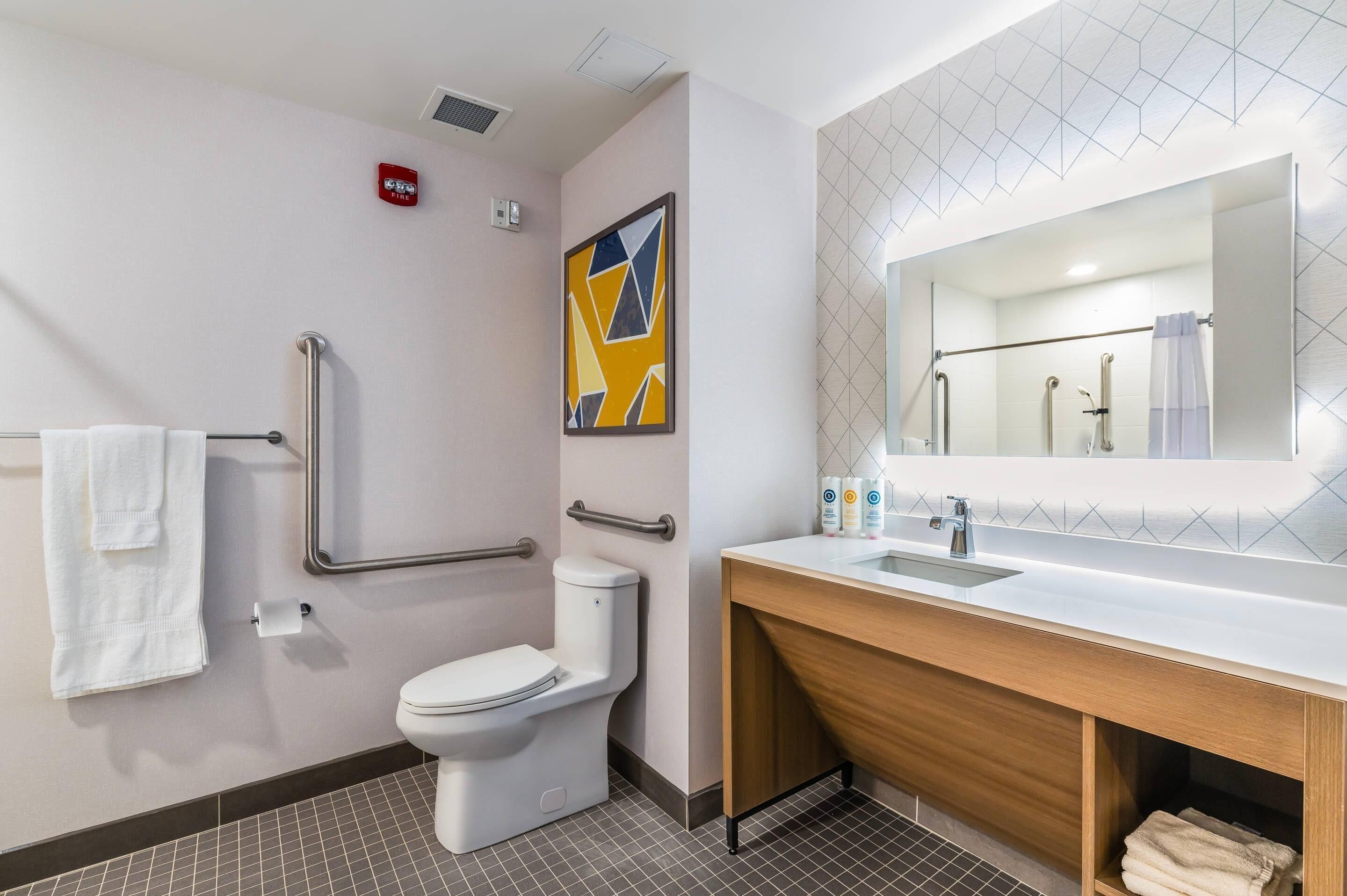 Un baño moderno con inodoro, barras de apoyo, lavabo y espejo.