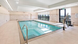 Une piscine intérieure à l’eau claire, équipée d’un escalier et offrant une vue sur l’extérieur grâce à de grandes fenêtres.