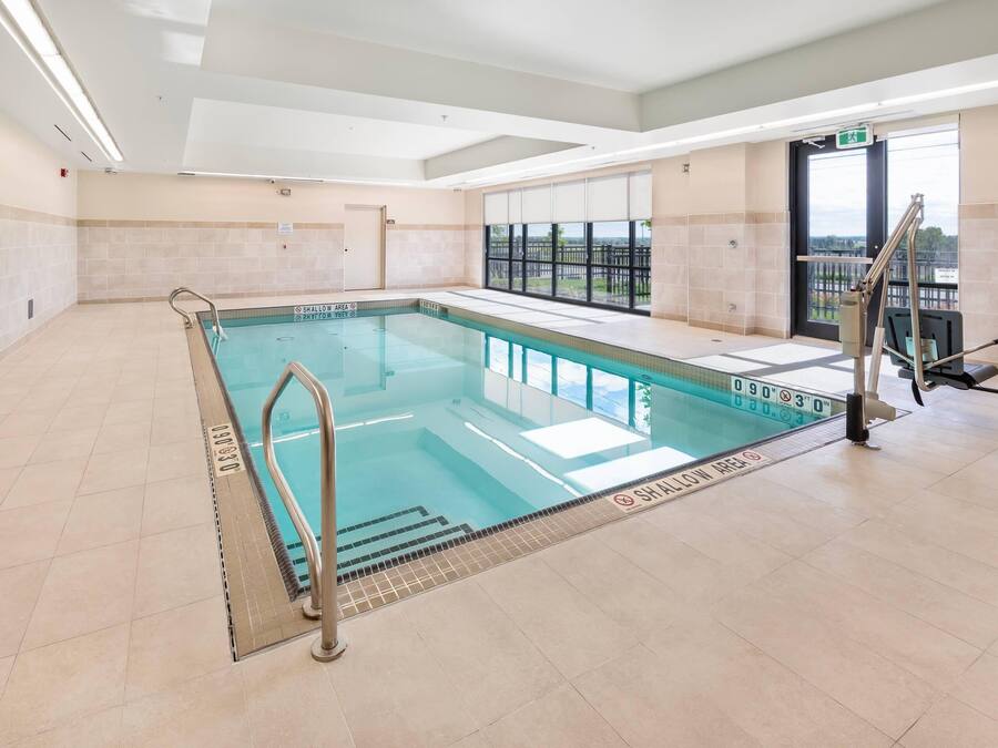An indoor swimming pool with clear water, a pool ladder, and a view of the outdoors through large windows.
