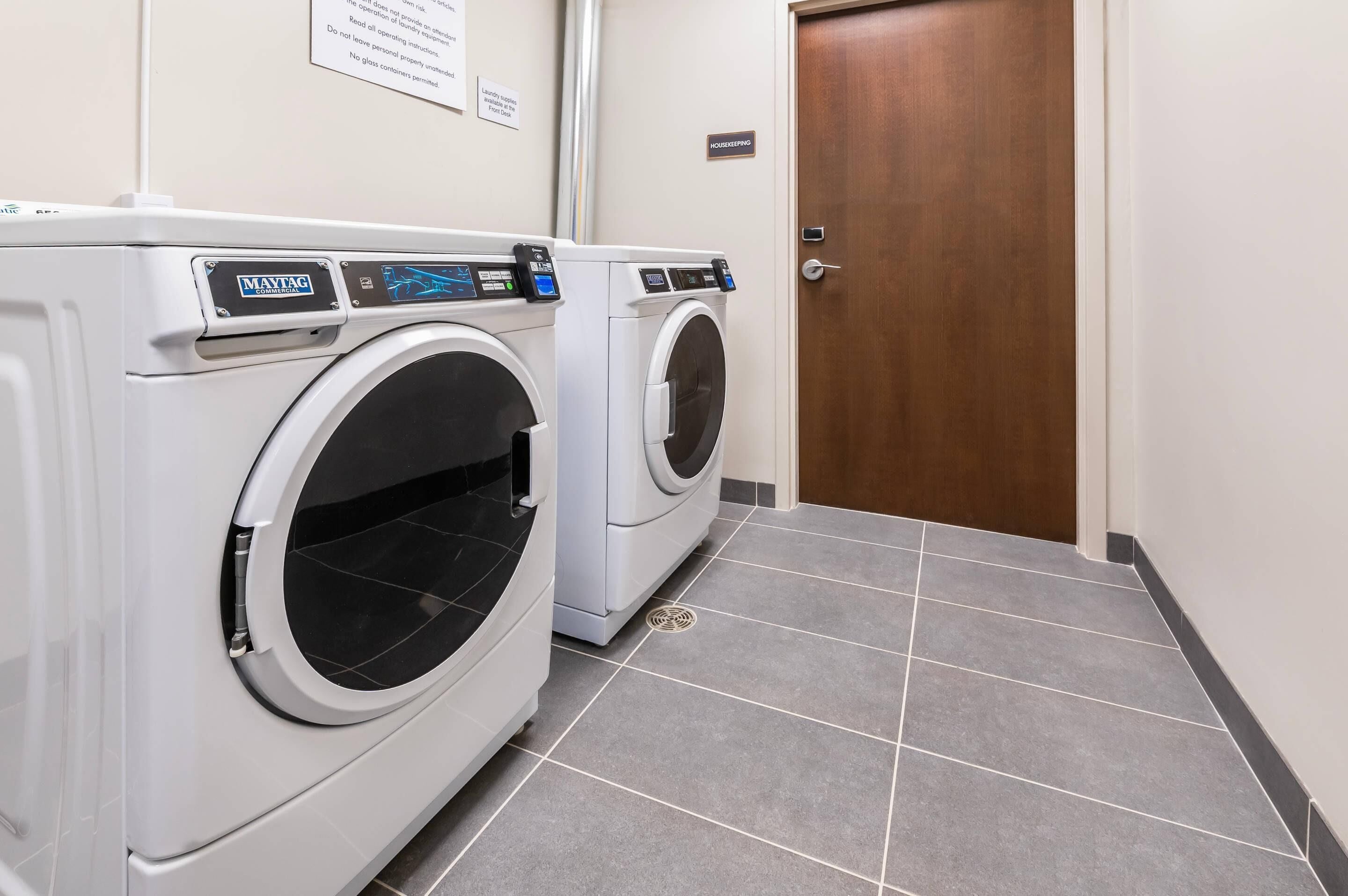 Un área de lavandería con dos lavadoras Maytag, piso de baldosas y puerta de madera.
